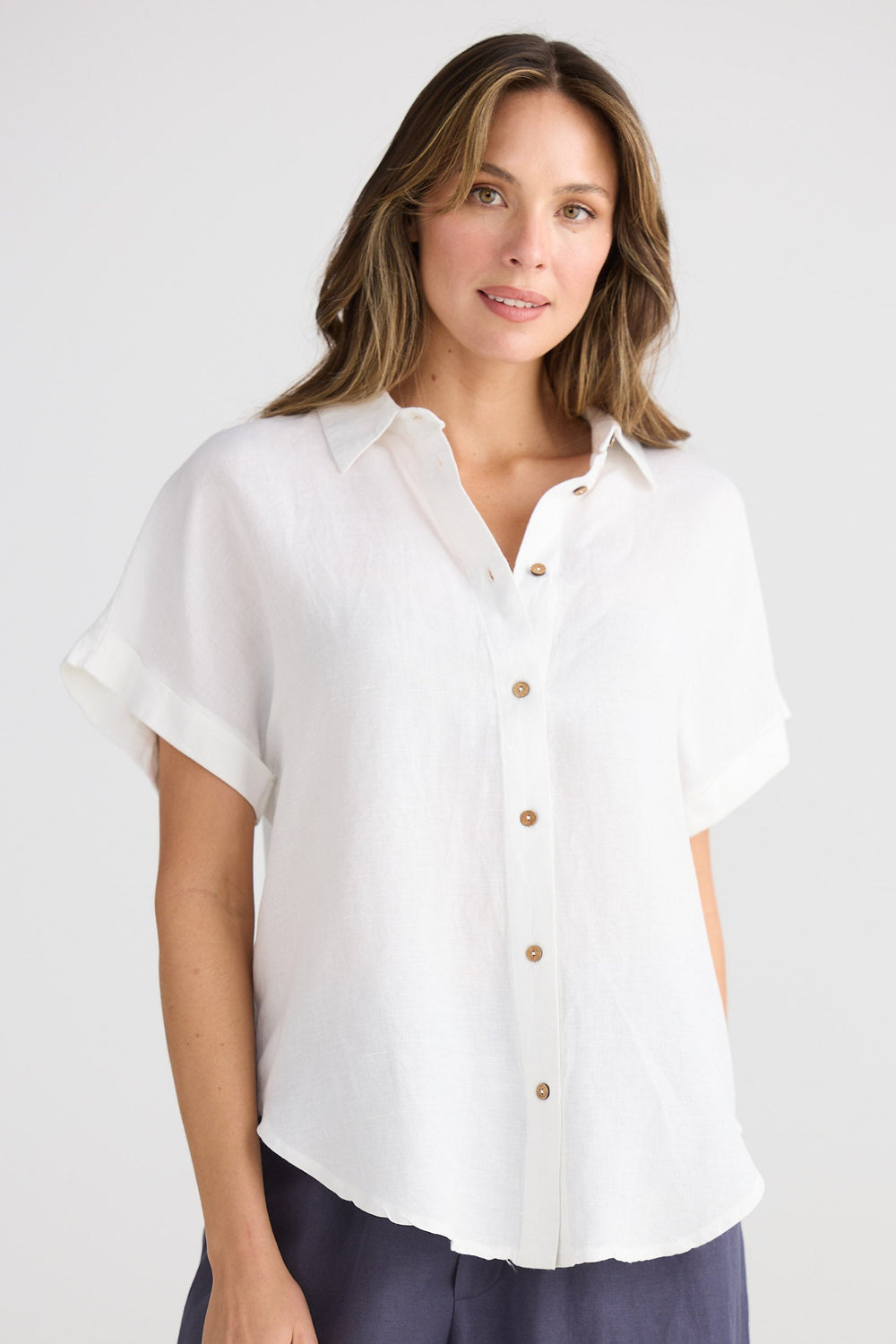 Woman wearing a white blouse with short sleeves and buttons, standing against a plain background