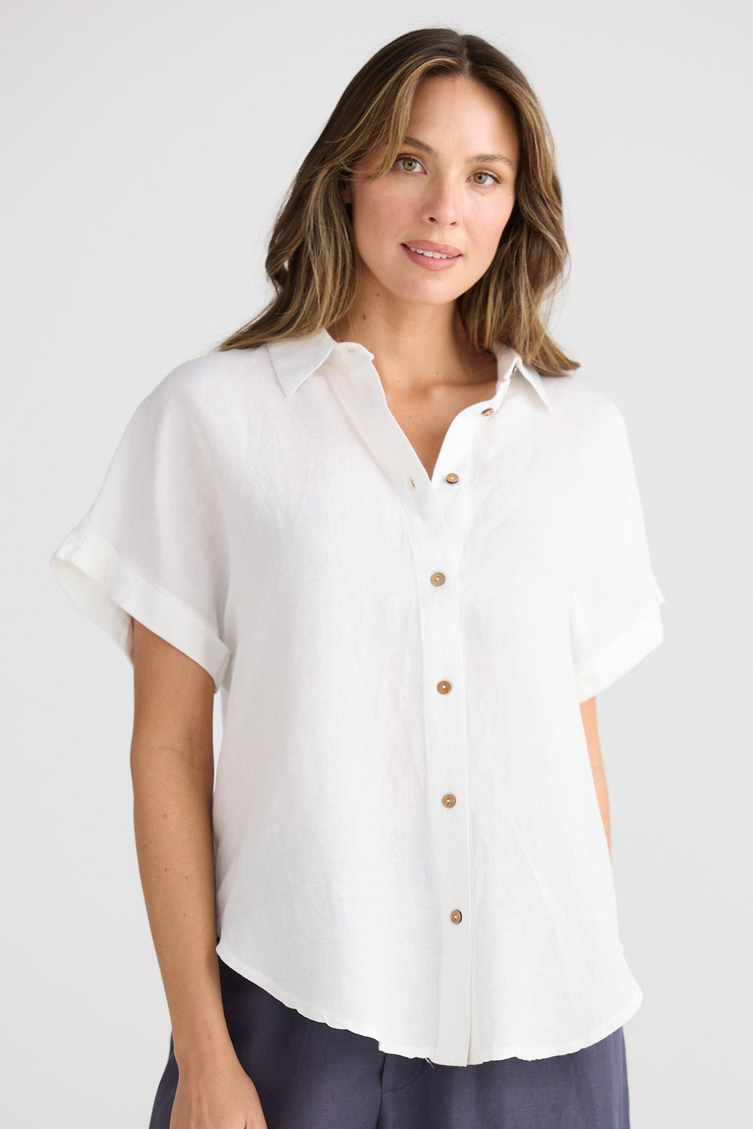 Woman wearing a white blouse with short sleeves and buttons, standing against a plain background