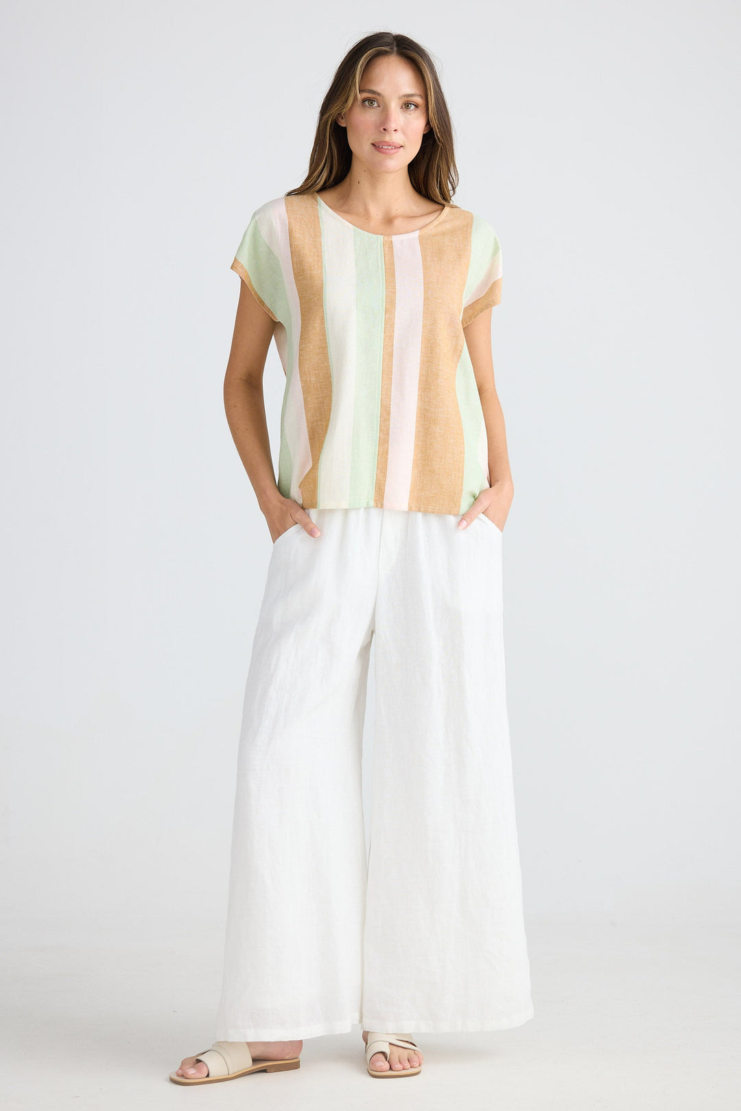 Woman wearing a multicolored striped top with white pants on a plain background