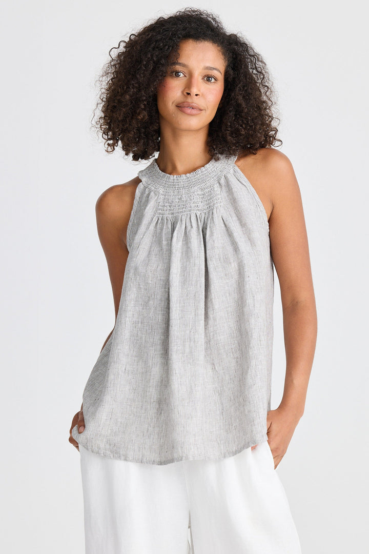 Woman wearing a gray sleeveless top and white pants on a white background