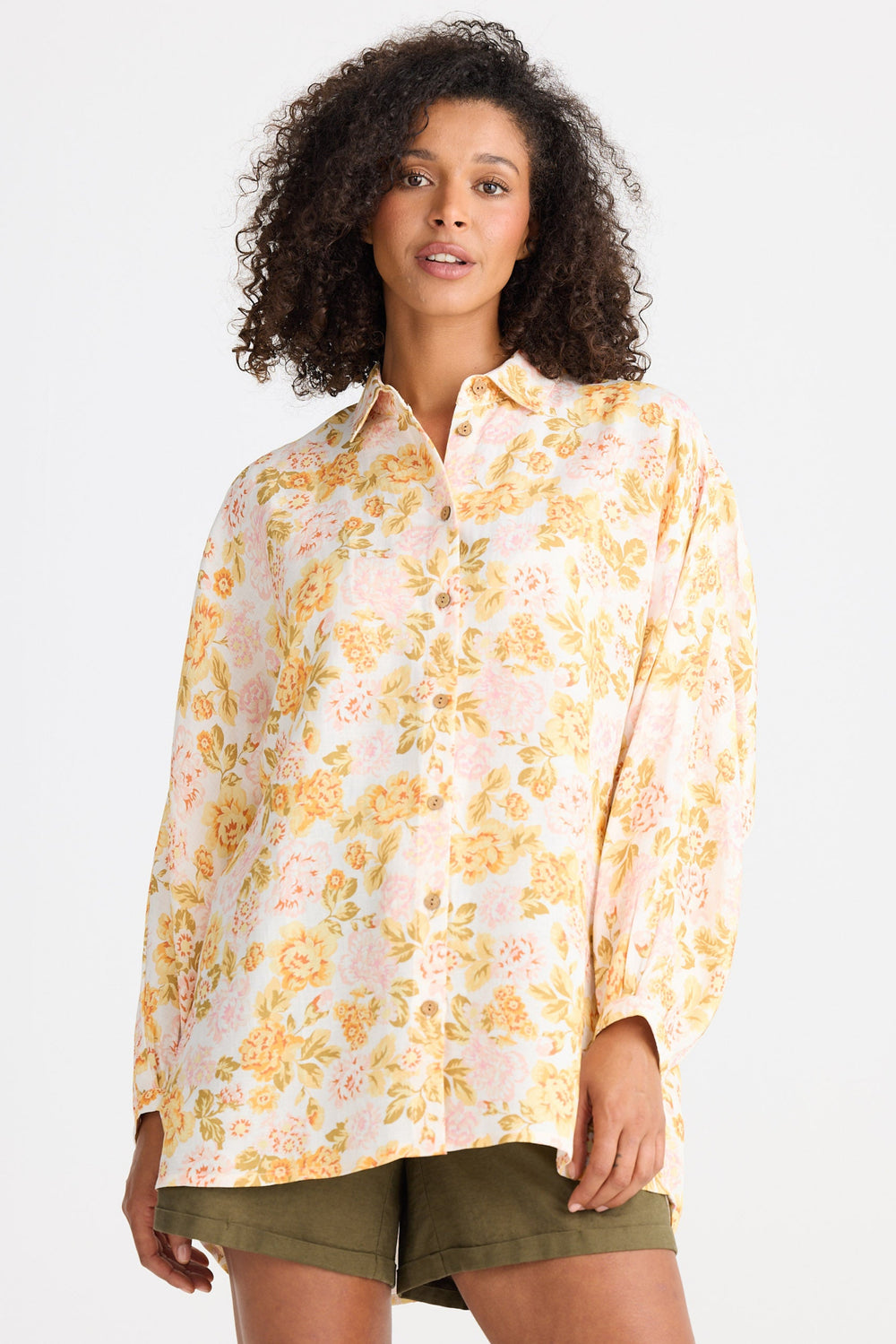 Woman wearing a yellow floral shirt and green shorts on a white background
