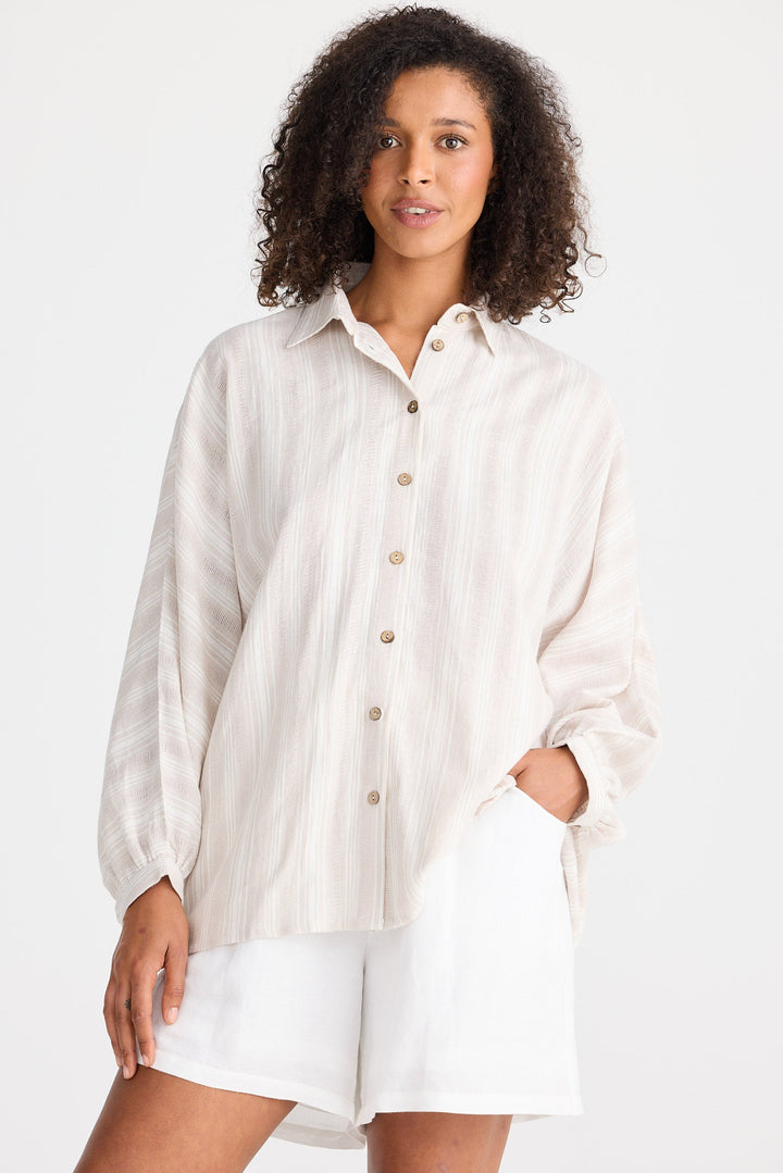 Woman wearing a light coloured striped button-up shirt and white shorts on a white background