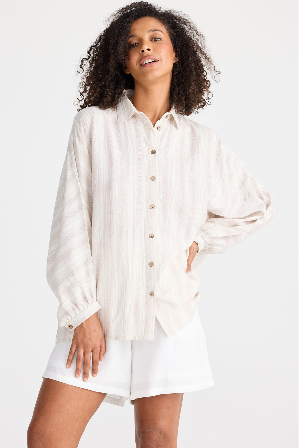 Woman wearing a light coloured striped button-up shirt and white shorts on a white background