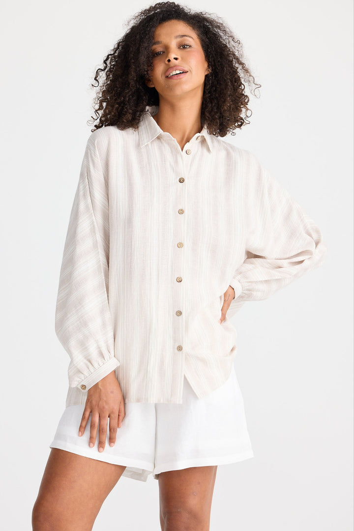 Woman wearing a light coloured striped button-up shirt and white shorts on a white background