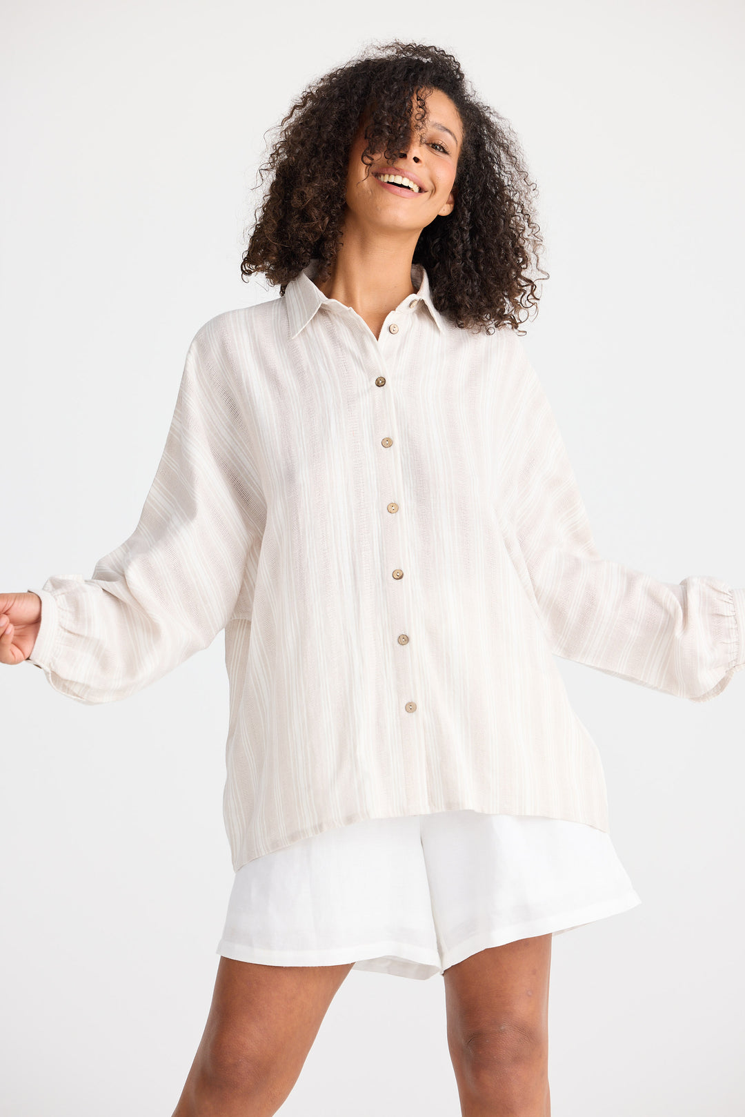 Woman wearing a light coloured striped button-up shirt and white shorts on a white background