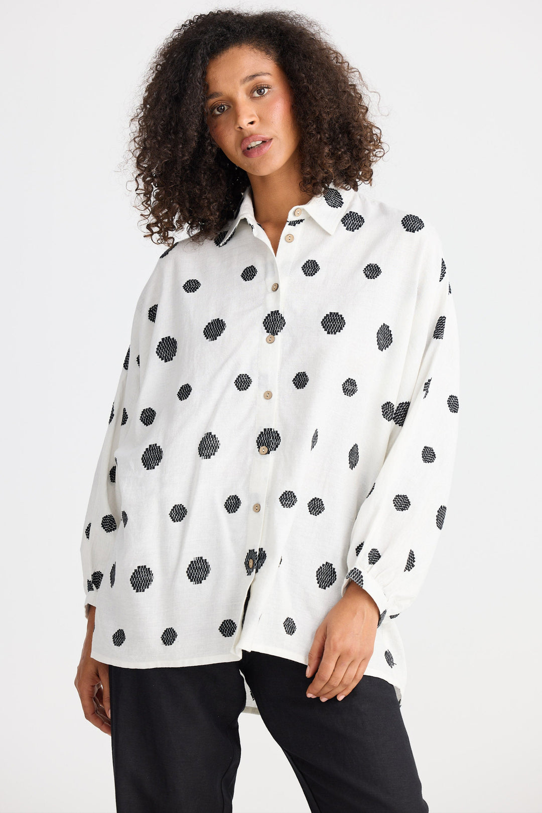 Woman wearing a white blouse with black polka dots on a plain background