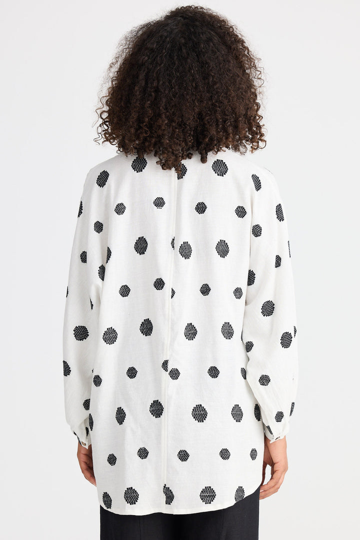 Person wearing a white blouse with black polka dots on a plain background