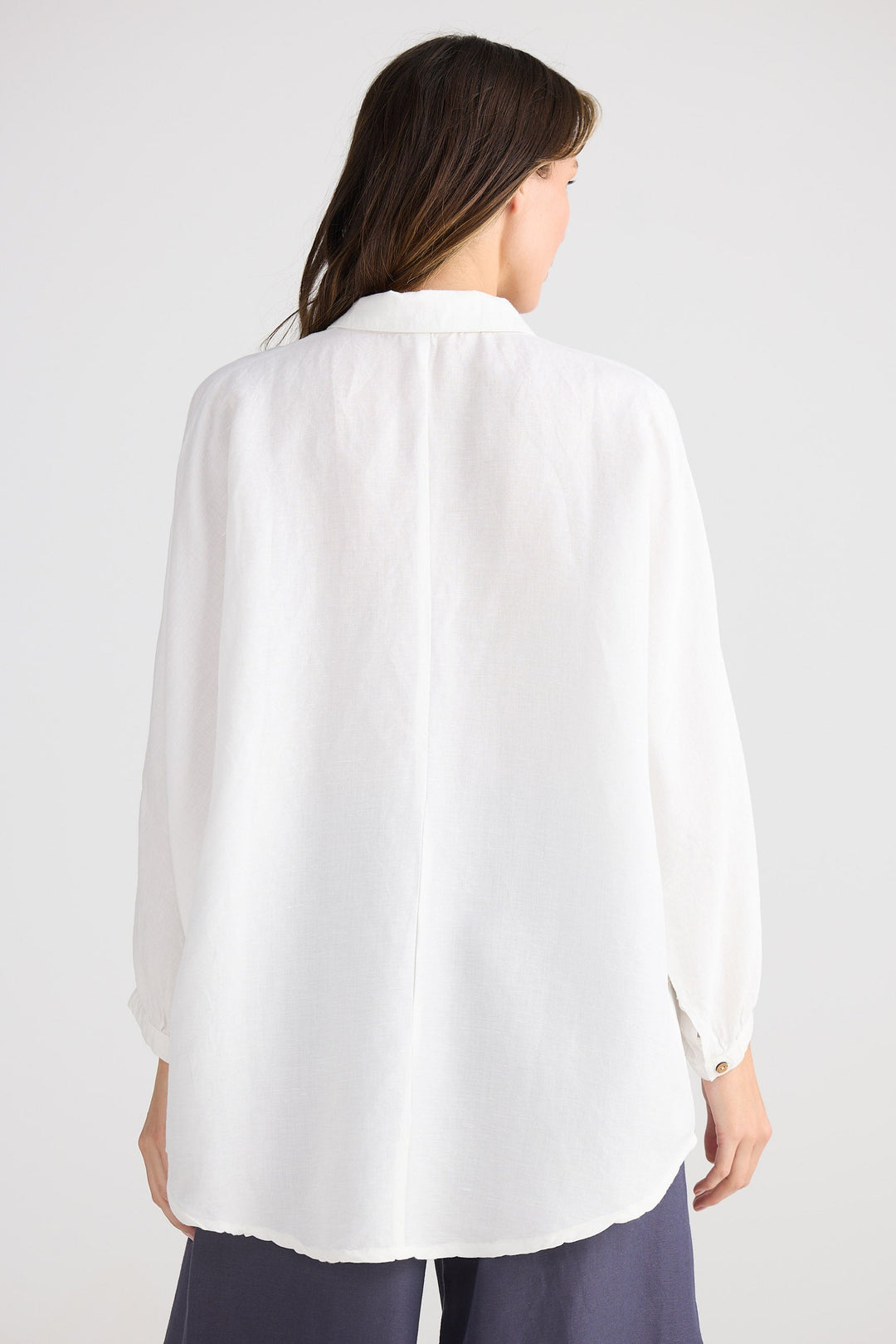 Person wearing a white shirt and dark pants on a plain background