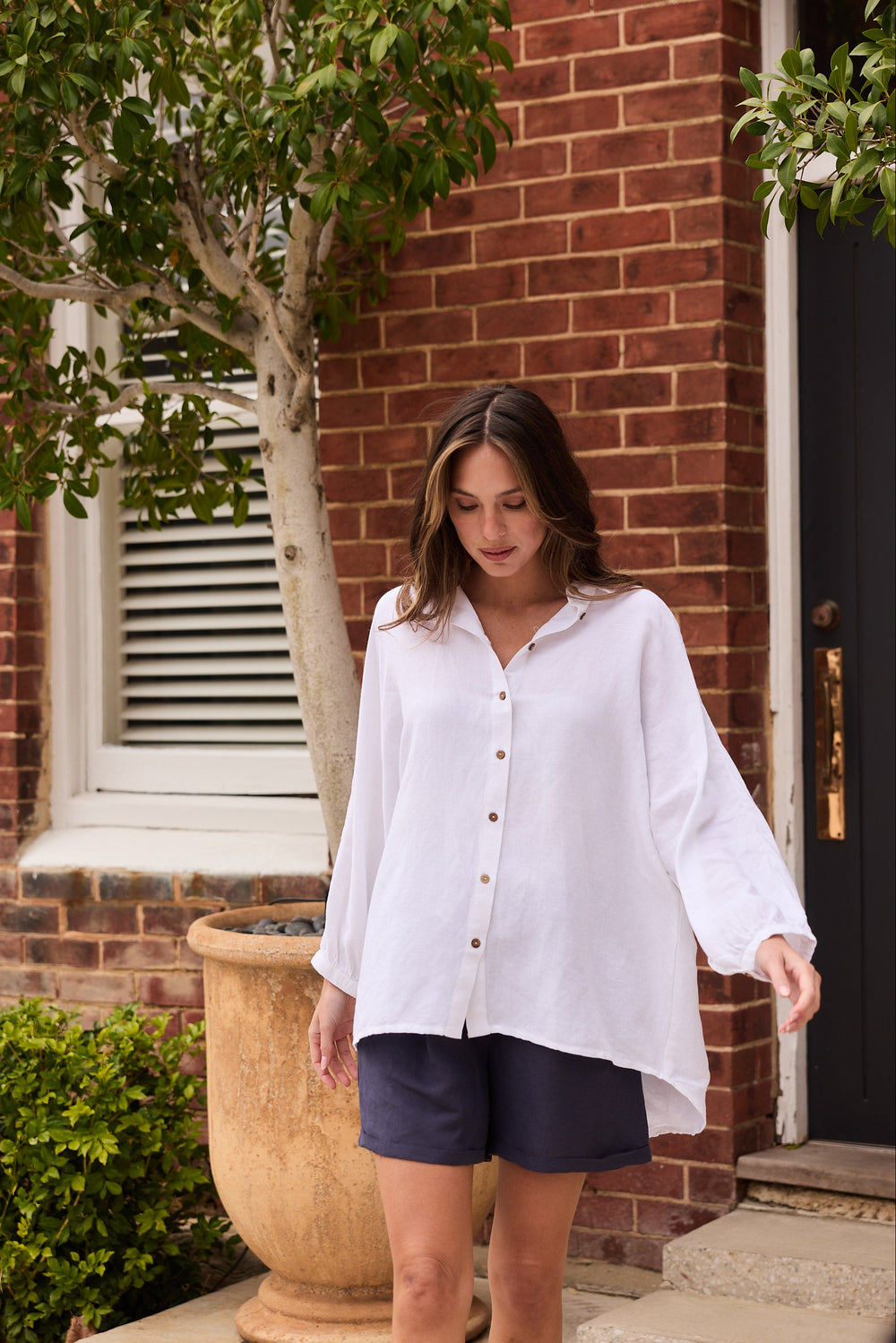 Woman in a white shirt and dark shorts standing outside a brick building.