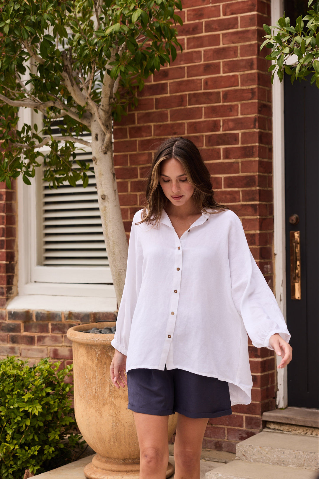 Woman in a white shirt and dark shorts standing outside a brick building.