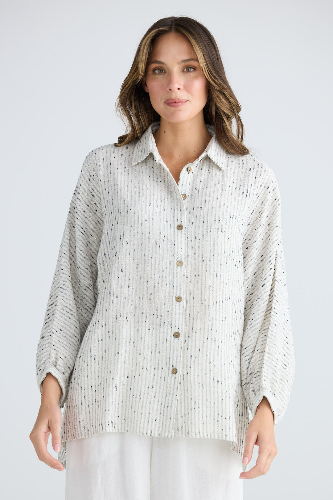 Woman wearing a light-colored button-up shirt and white pants on a plain background