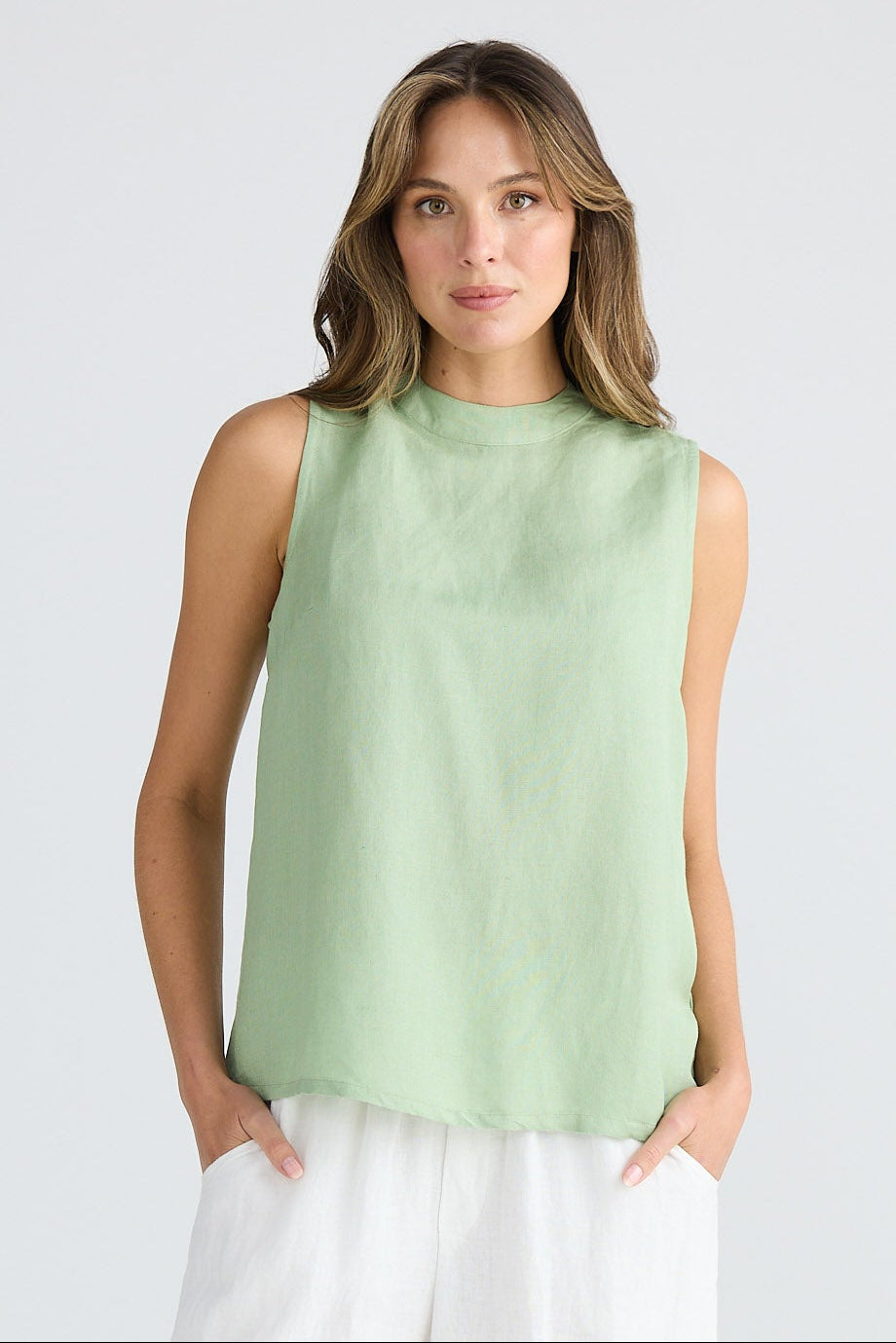 Woman wearing a light green sleeveless top and white pants on a white background