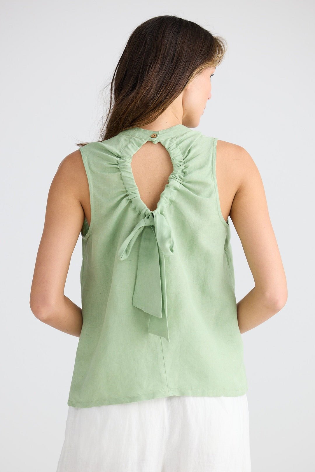 Woman wearing a light green sleeveless top with a bow detail on a white background