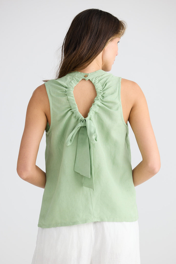 Woman wearing a light green sleeveless top with a bow detail on a white background