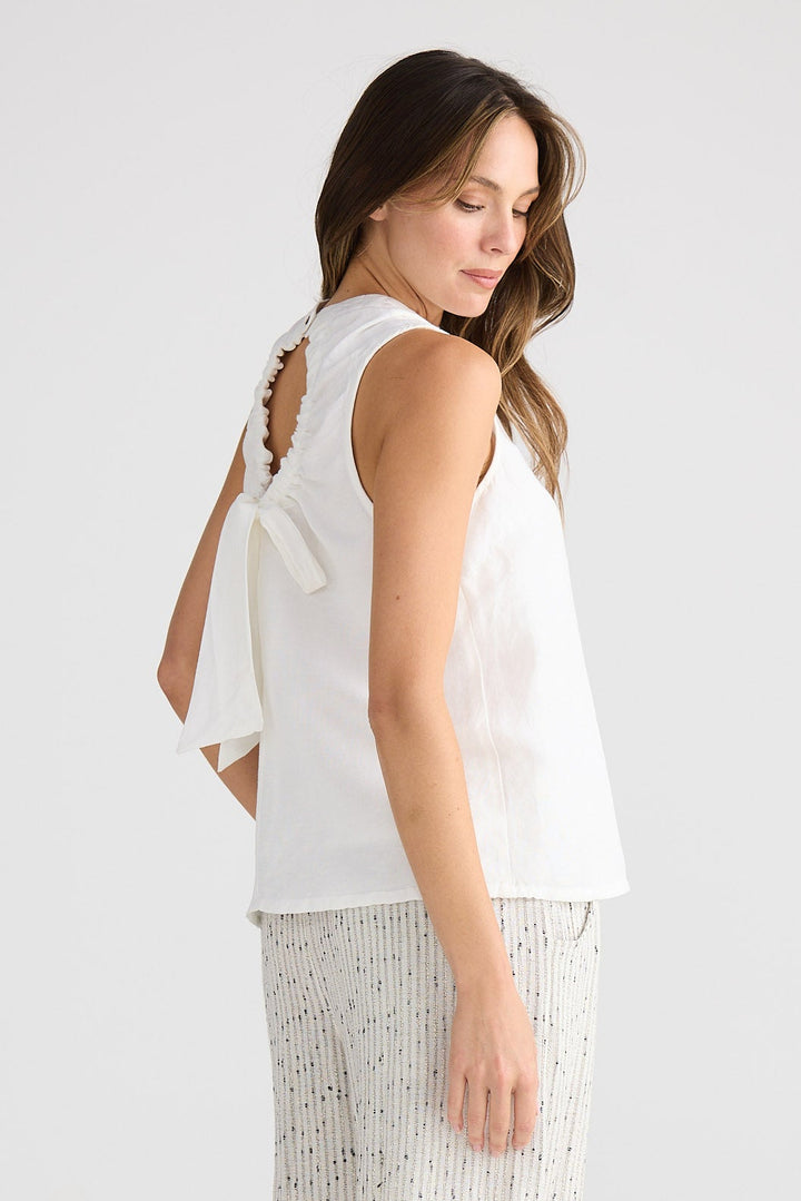 Woman wearing a white sleeveless top and patterned pants on a plain background