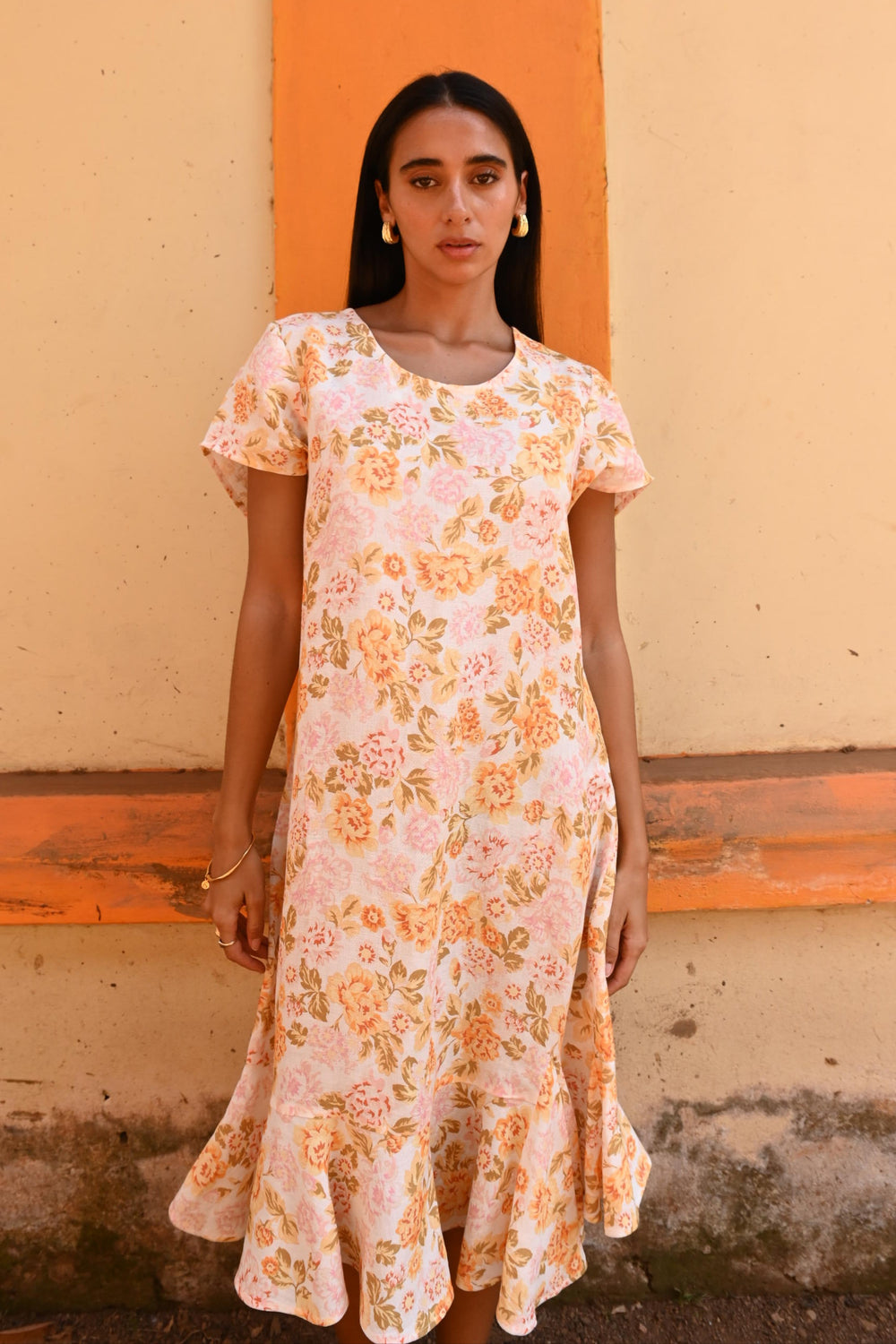 Woman wearing a floral dress standing against a wall with an orange stripe.