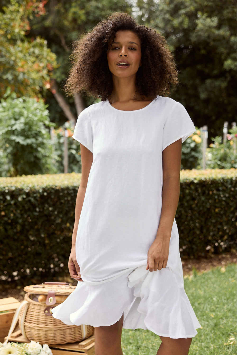 Woman wearing a white dress standing outdoors with greenery in the background