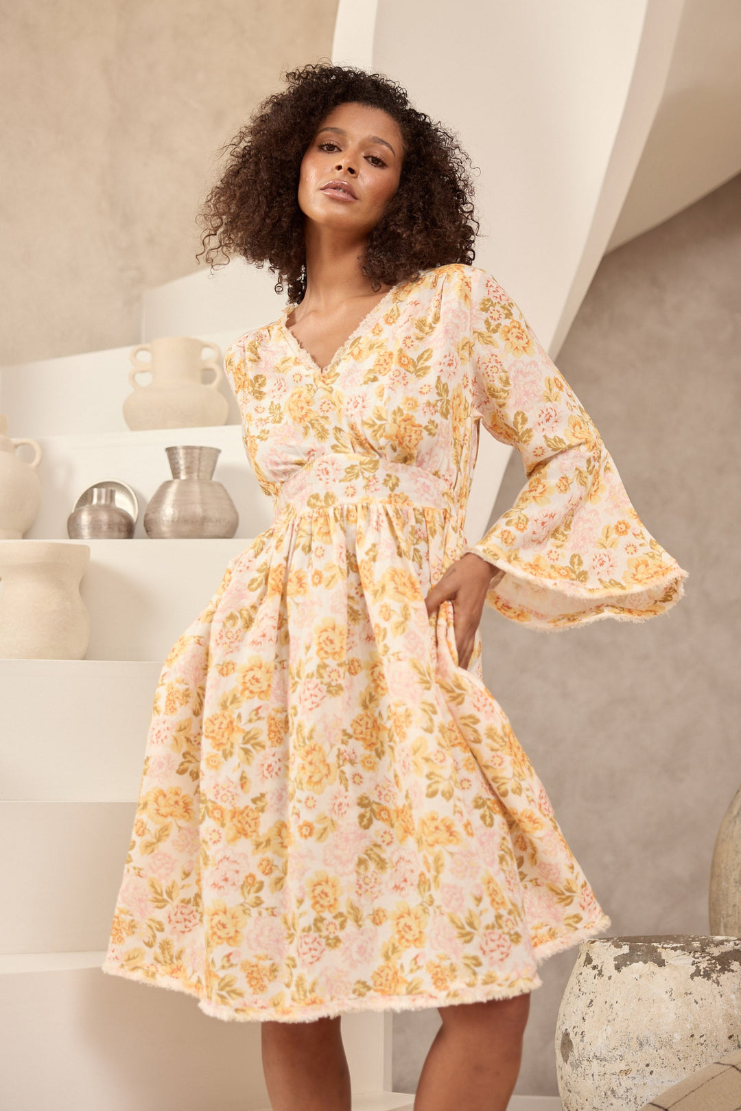 Woman wearing a floral dress standing in a room with decorative items.