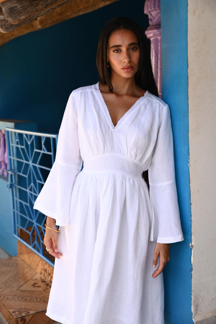 Woman in a white dress leaning on a blue wall with a patterned gate in the background