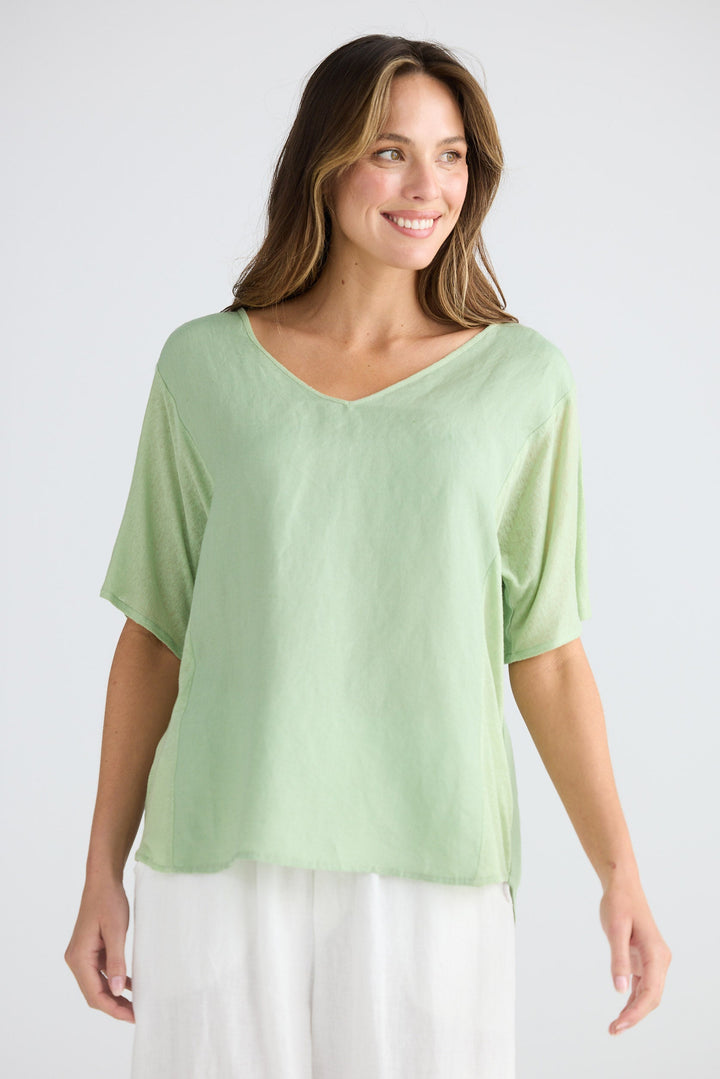 Woman wearing a light green top and white pants on a plain background