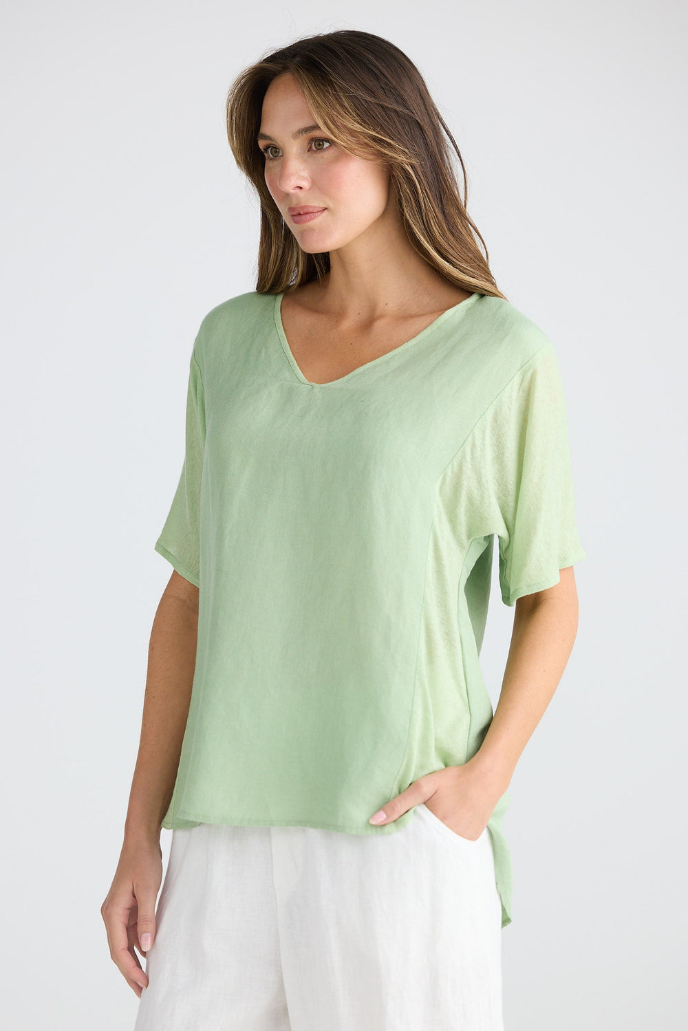 Woman wearing a light green top and white pants on a plain background