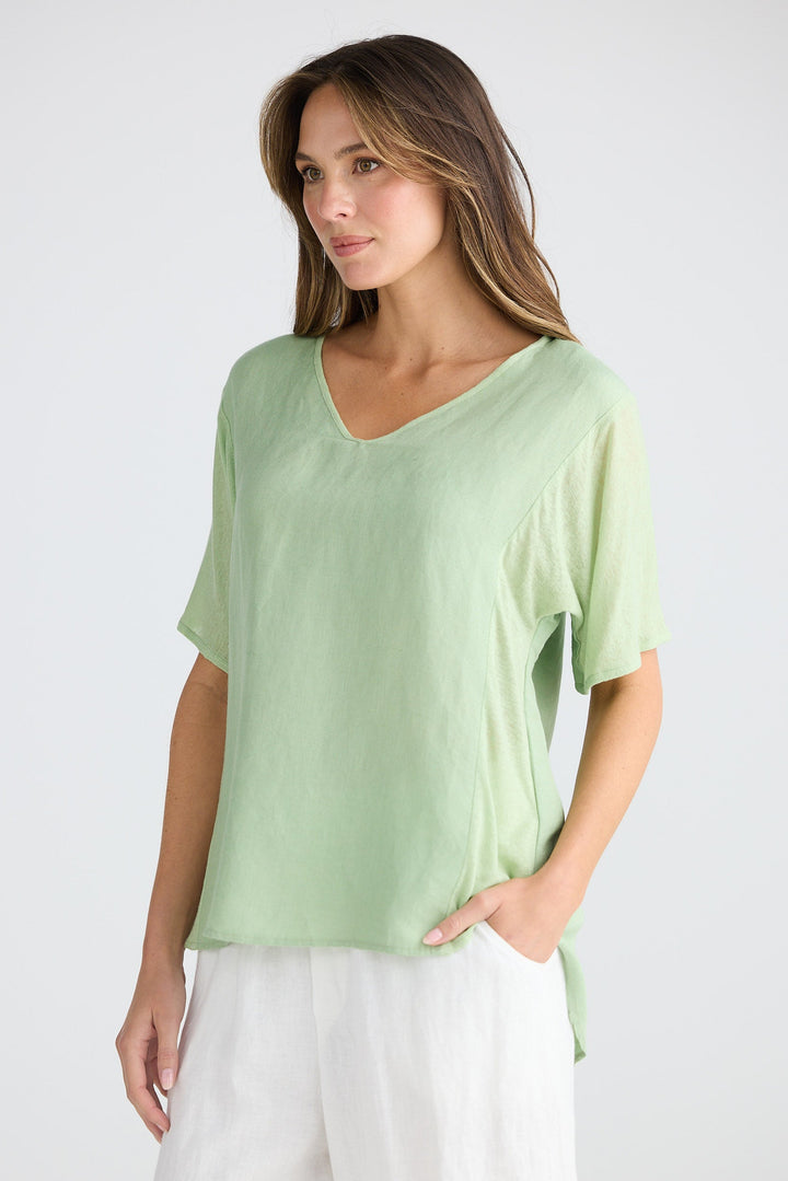 Woman wearing a light green top and white pants on a plain background