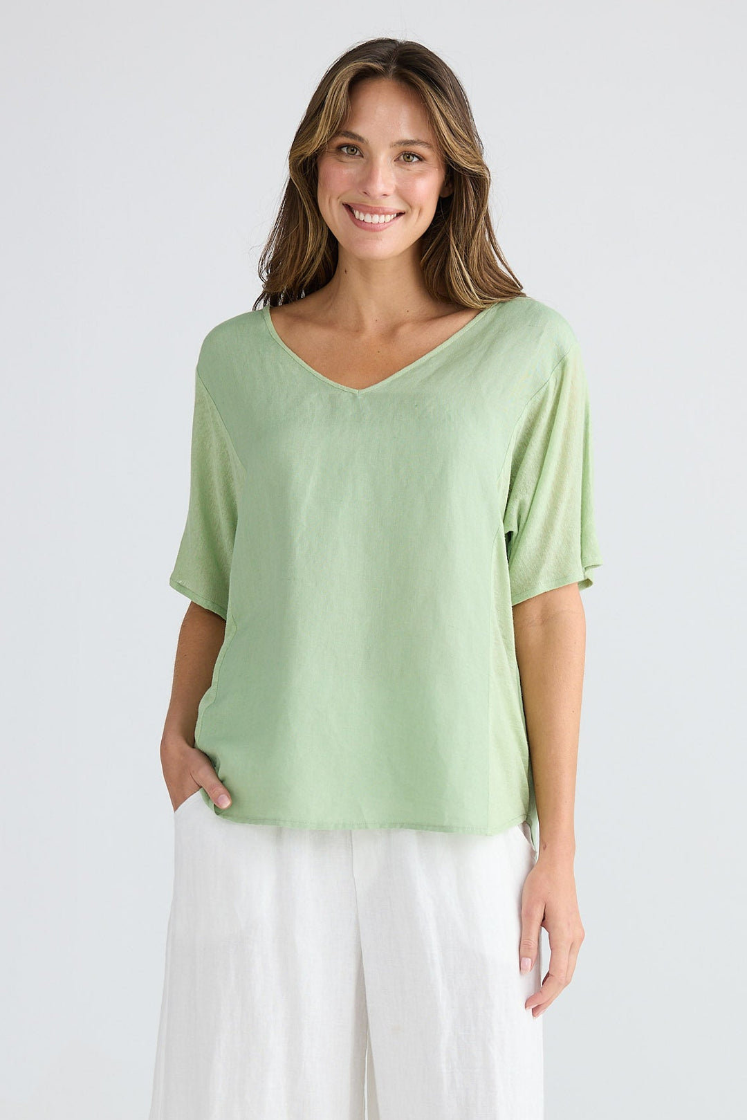 Woman wearing a light green top and white pants on a white background