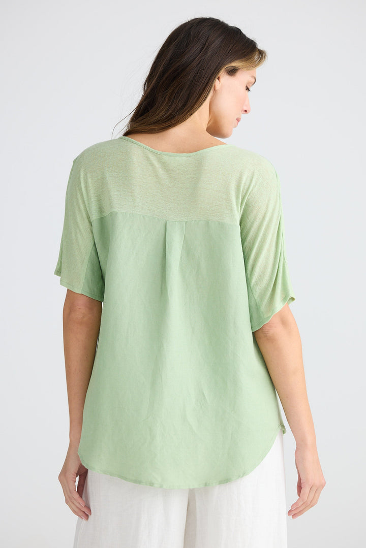 Woman wearing a light green top and white pants on a plain background