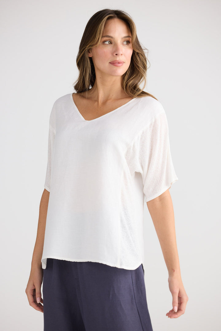 Woman wearing a white blouse and dark pants on a plain background