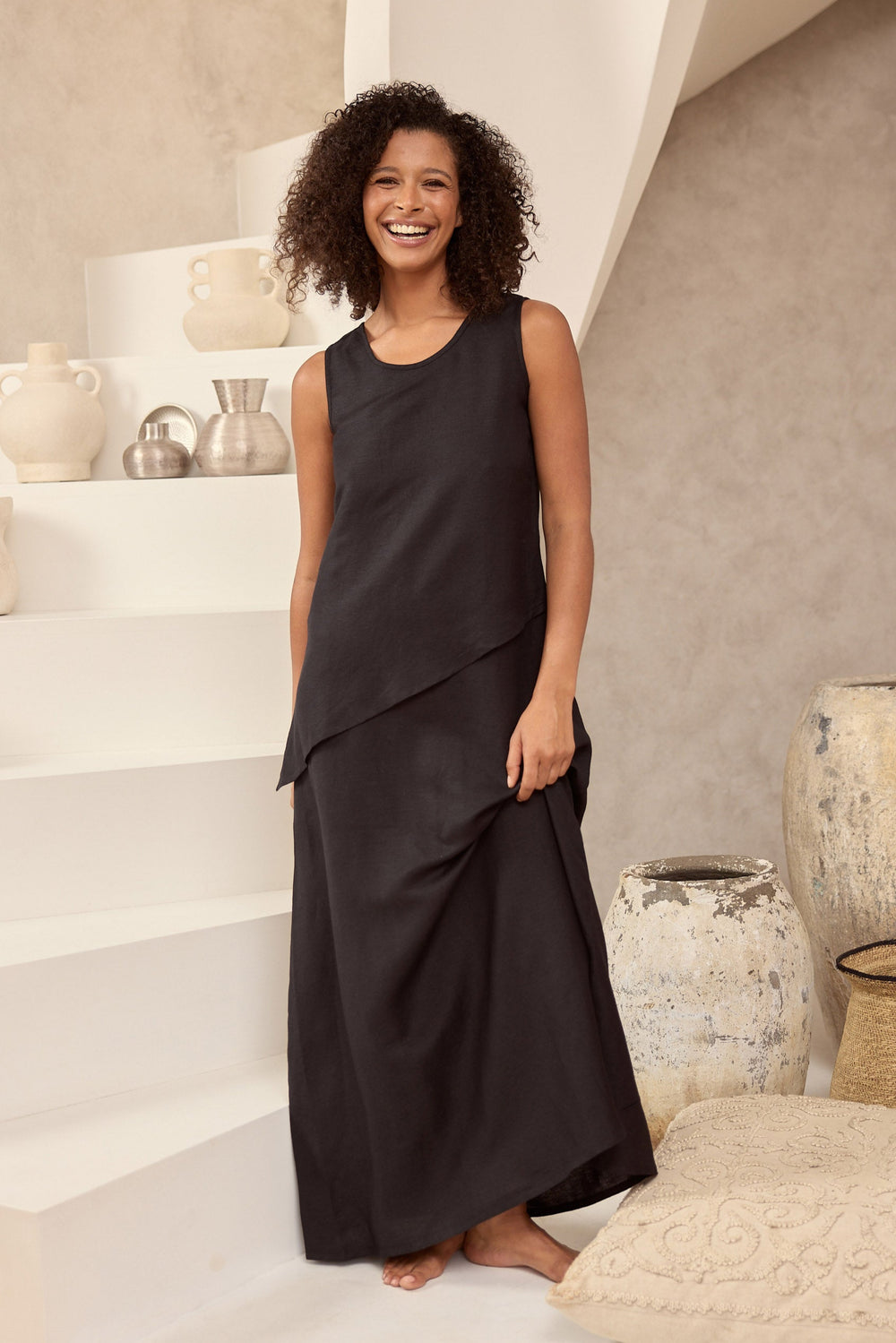 Woman in a black dress standing in a room with white walls and decorative vases.