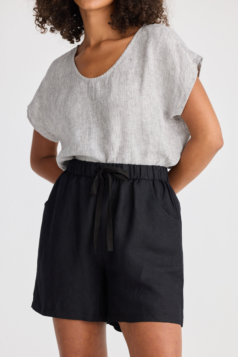 Person wearing a light gray top and black shorts on a white background