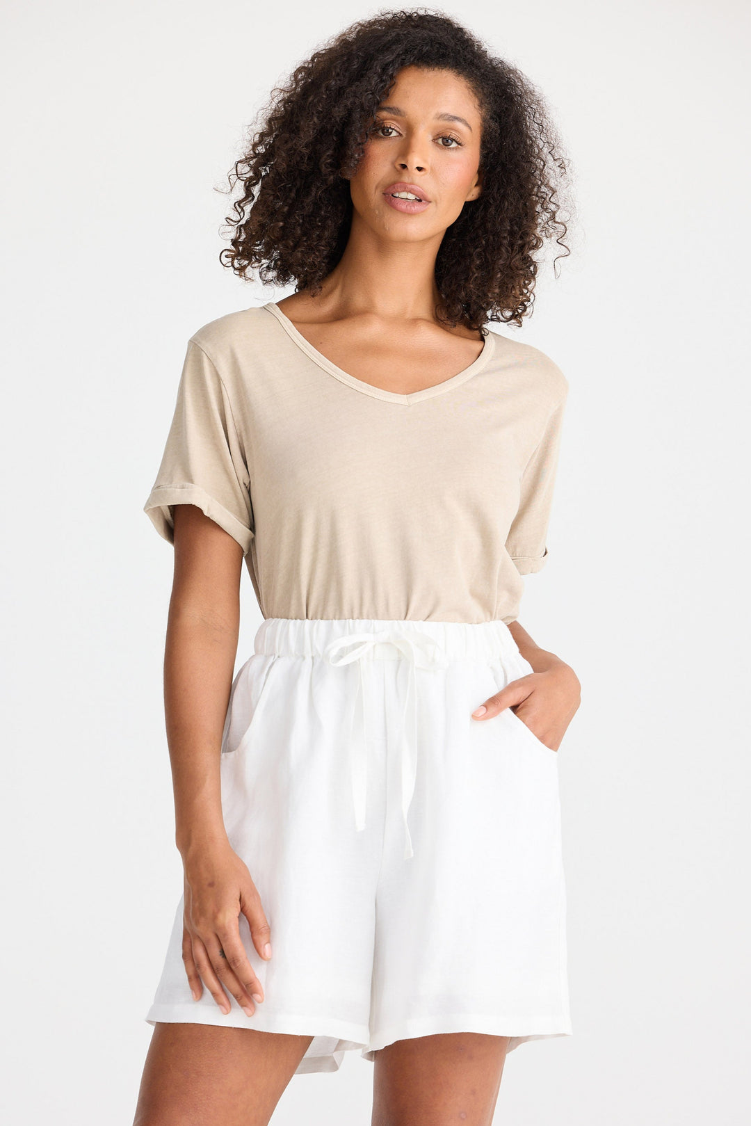 Woman wearing a beige top and white shorts on a white background