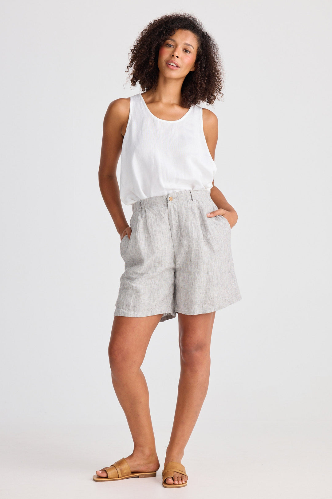 Woman wearing a white sleeveless top and light gray shorts on a white background