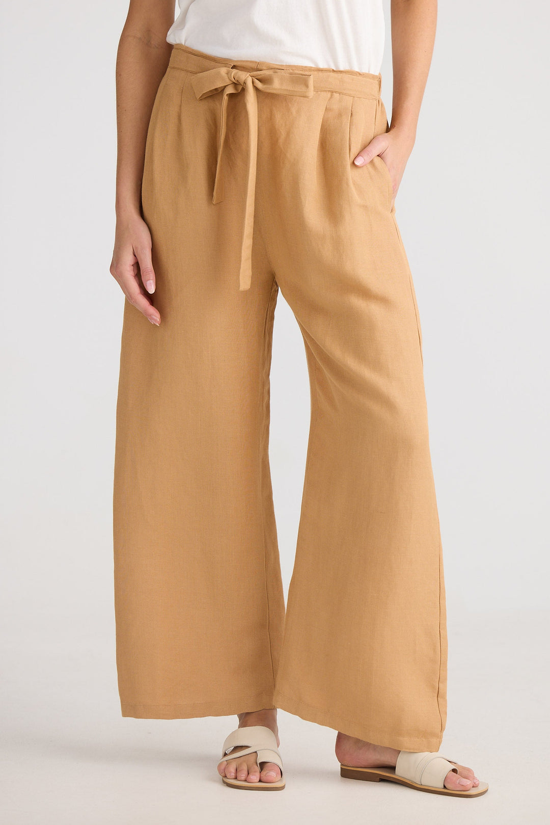 Person wearing tan wide-leg pants with a white top on a plain background