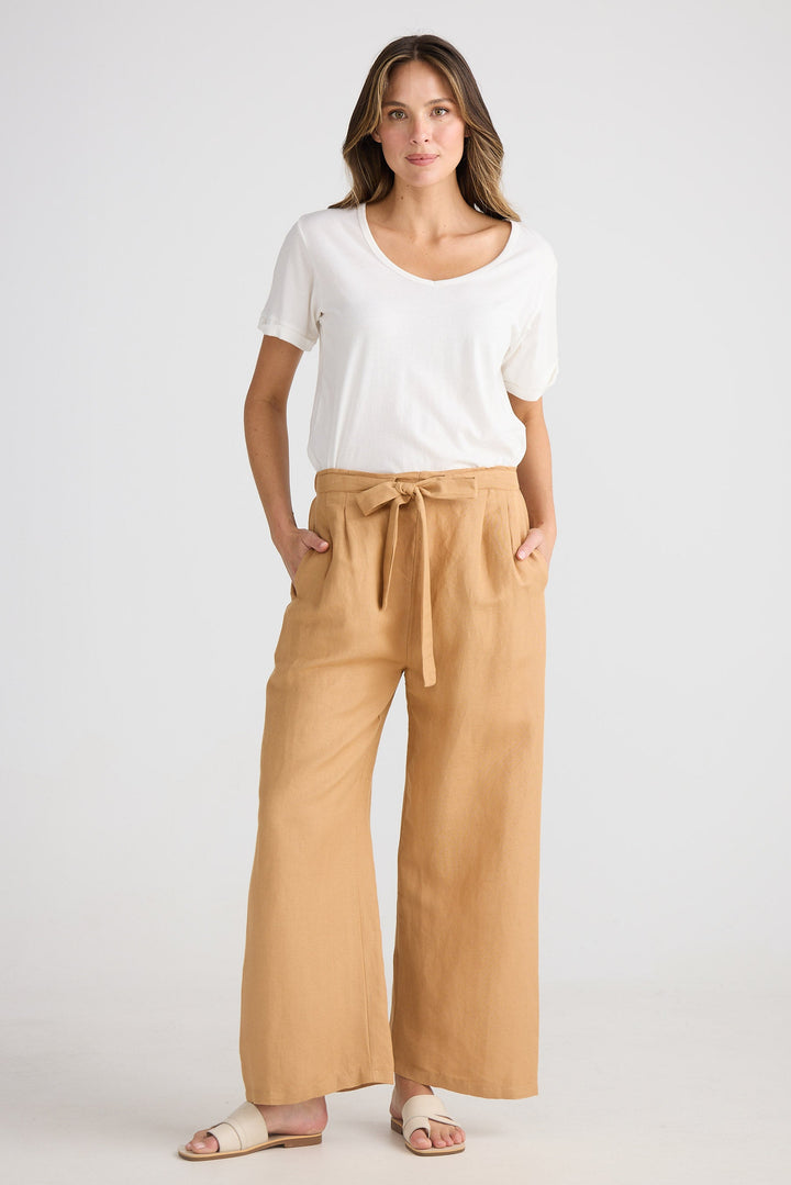 Woman wearing a white top and tan pants on a plain background