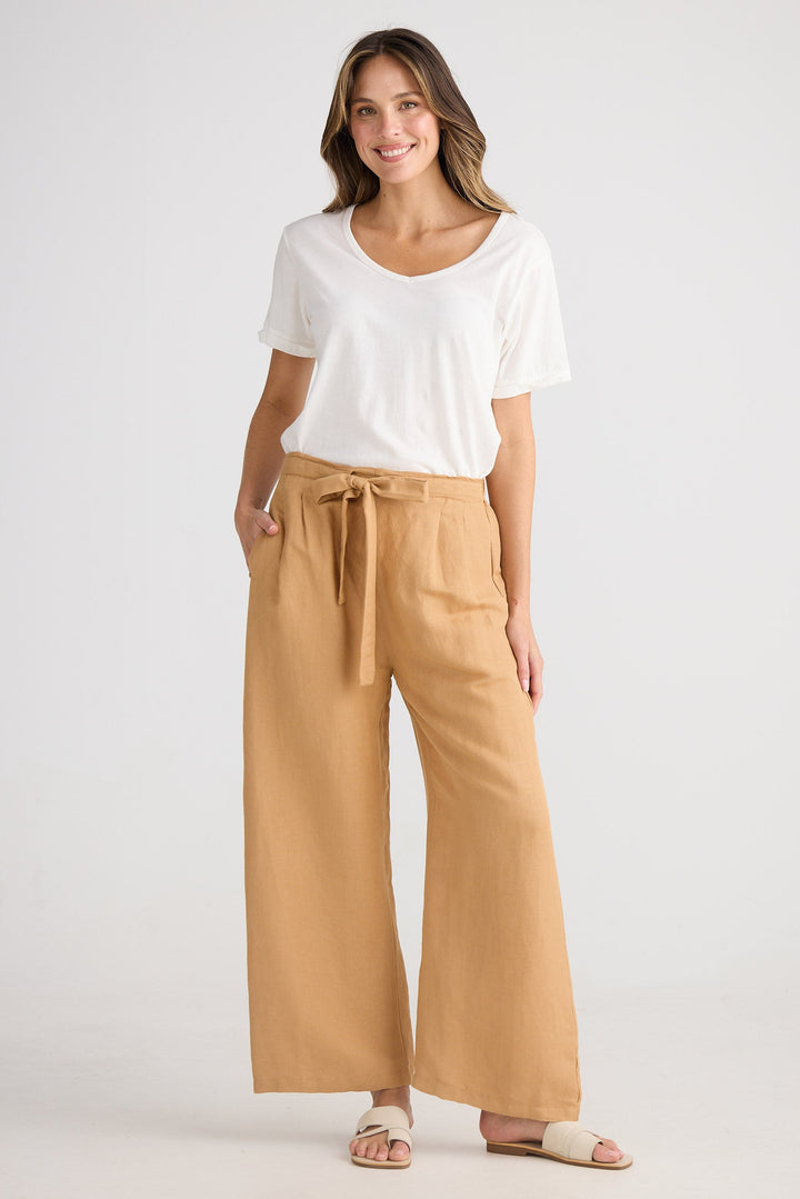 Woman wearing a white top and tan wide-leg pants on a white background