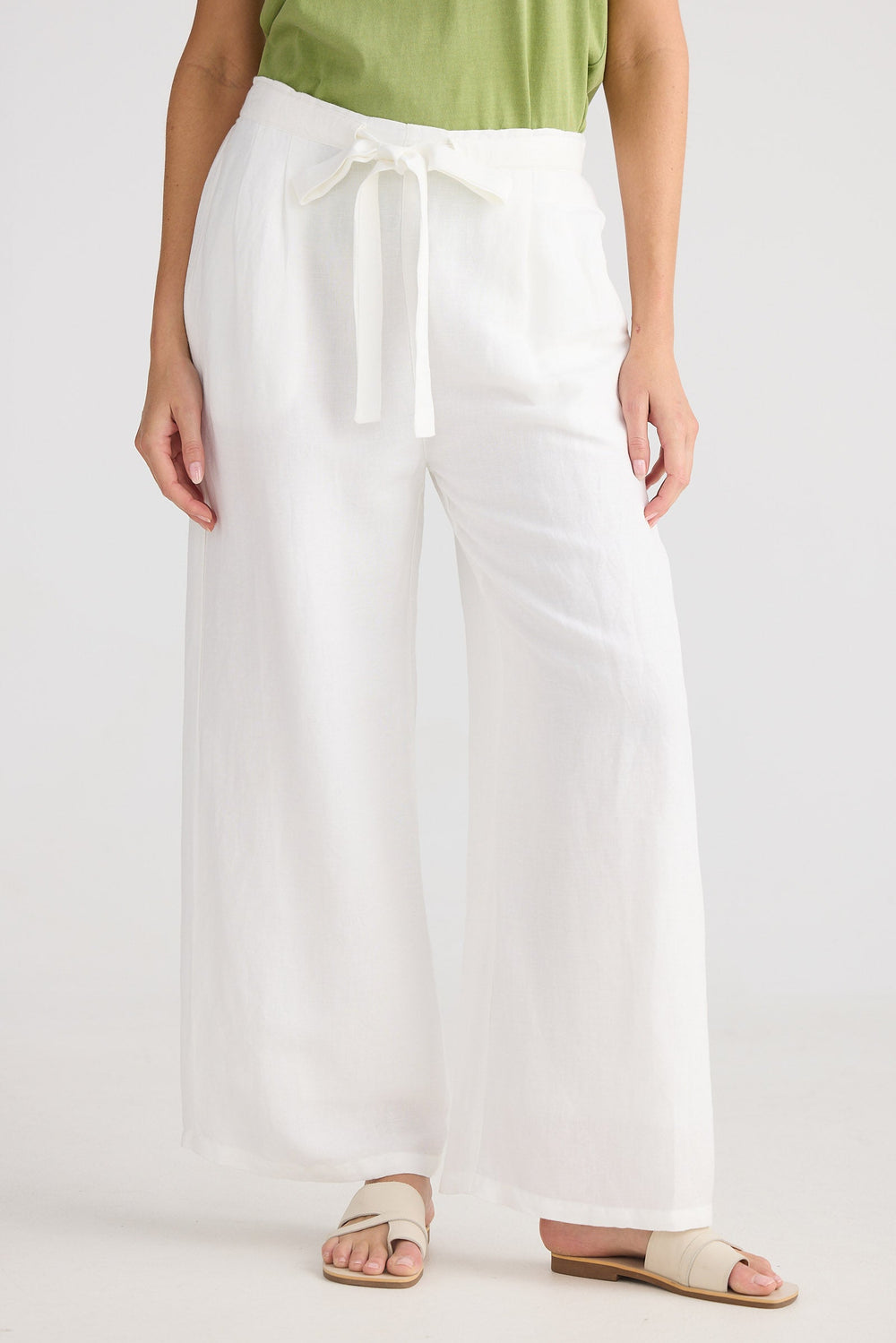 Person wearing a green top and white wide-leg pants on a plain background