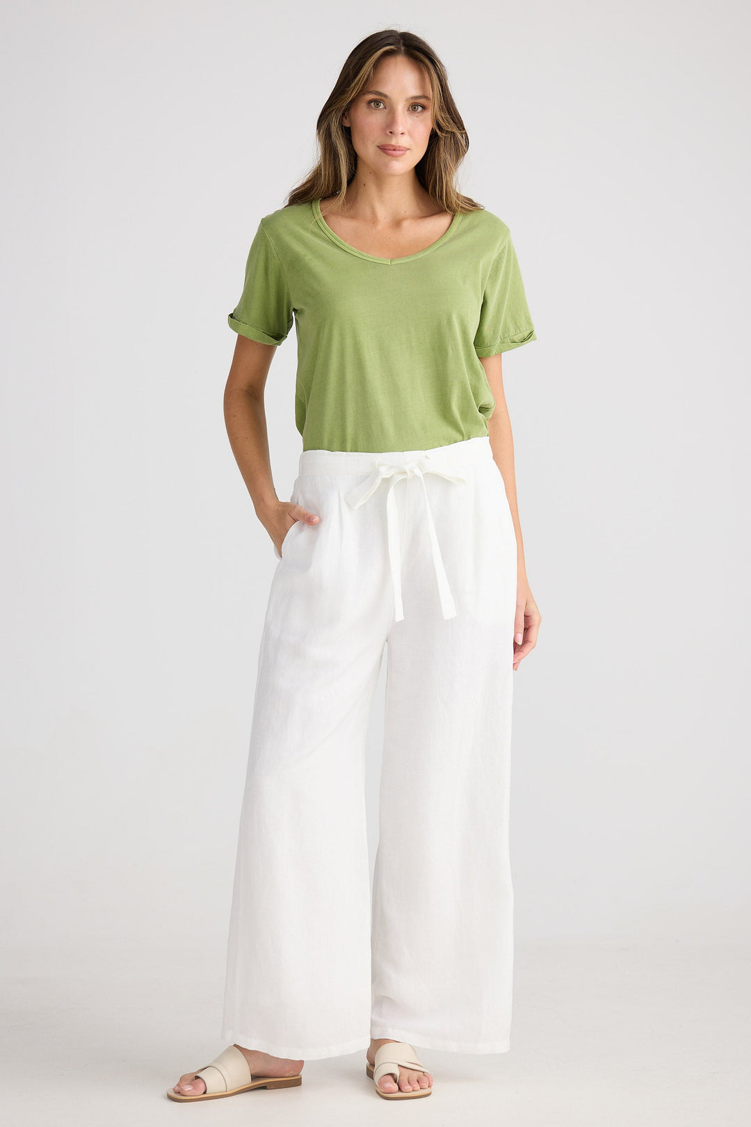 Woman wearing a green top and white pants on a plain background