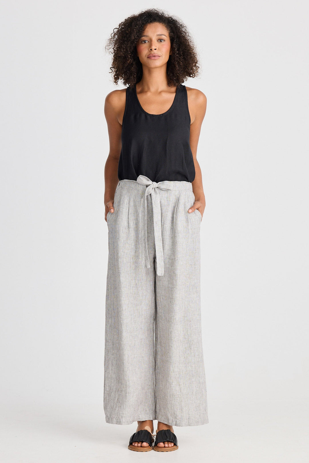 Woman wearing a black sleeveless top and light gray wide-leg pants on a white background