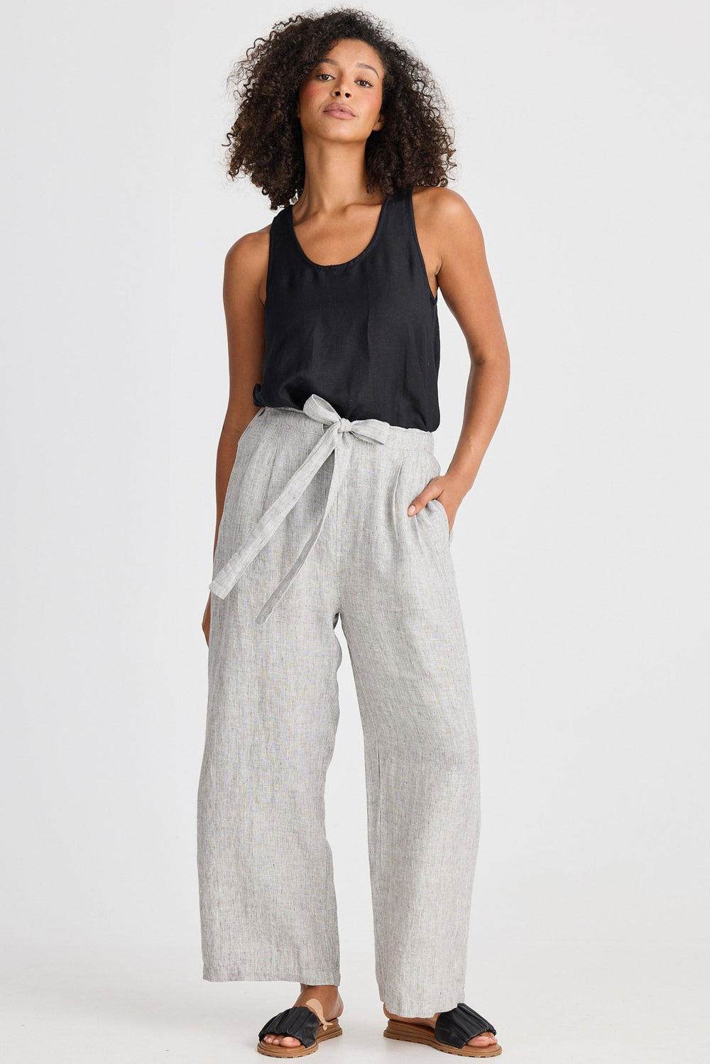Woman wearing a black sleeveless top and light gray wide-leg pants on a white background