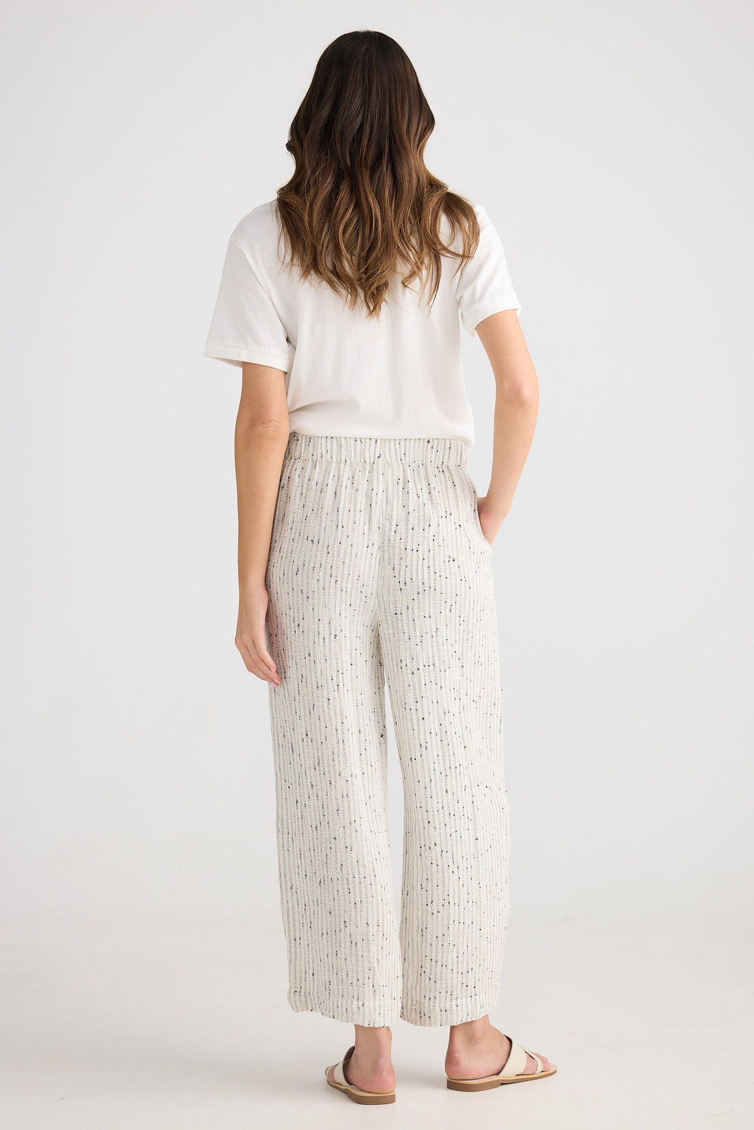 Woman wearing a white t-shirt and light-colored wide-leg pants on a plain background