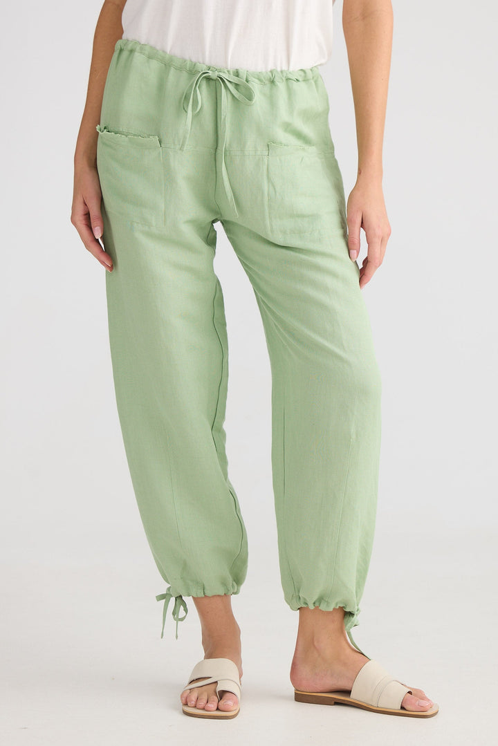 Person wearing light green pants with a white top on a plain background