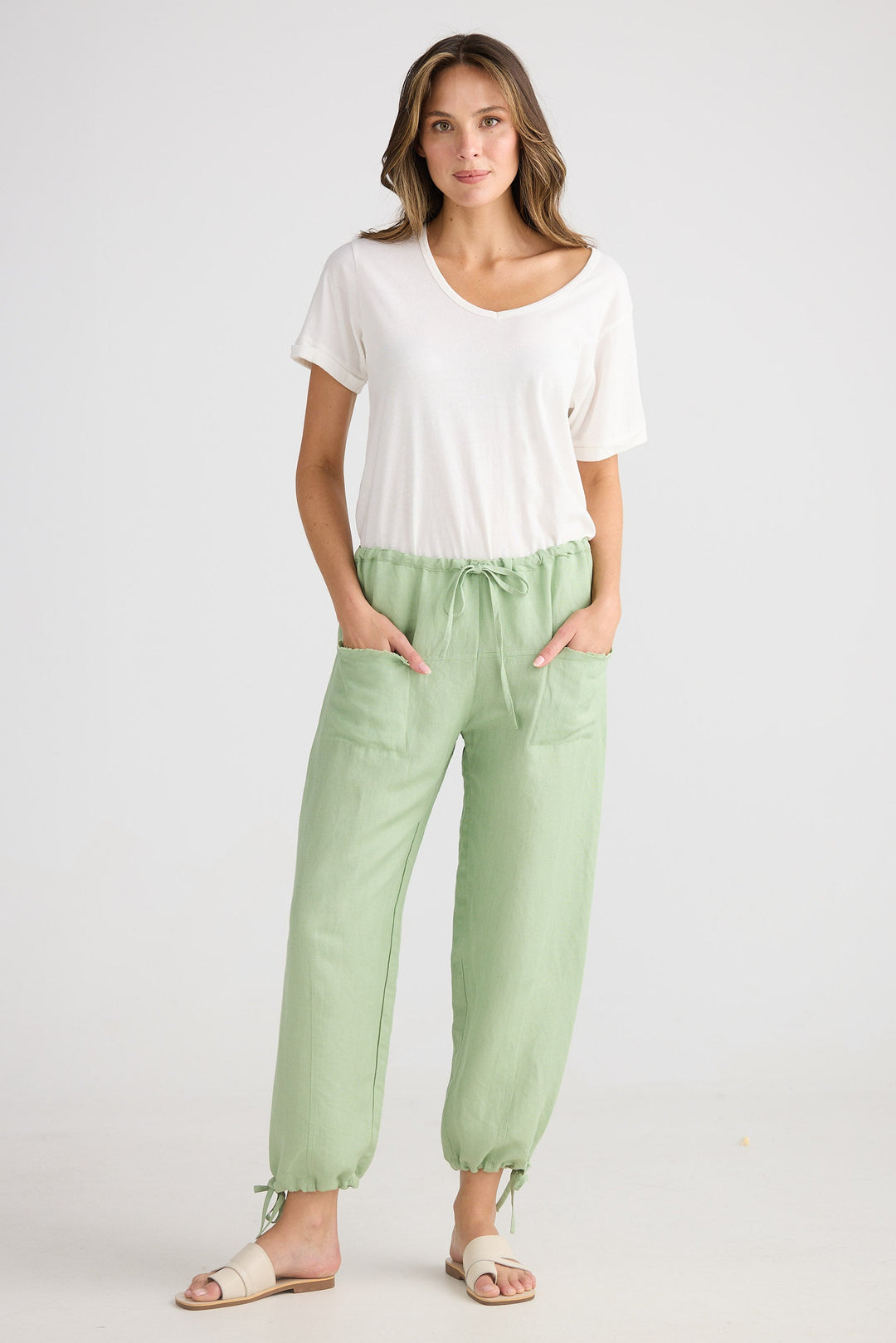 Woman wearing a white top and light green pants on a white background