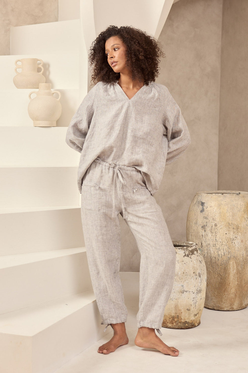 Woman in a light gray top and pant set standing on a staircase in a minimalistic room.