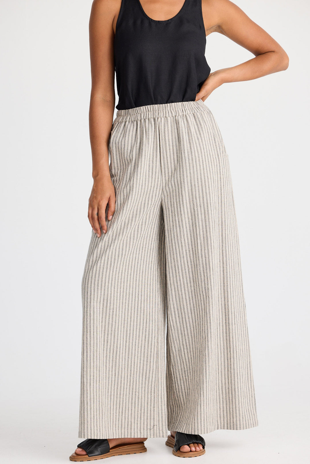 Woman wearing a black tank top and wide-leg striped pants on a white background