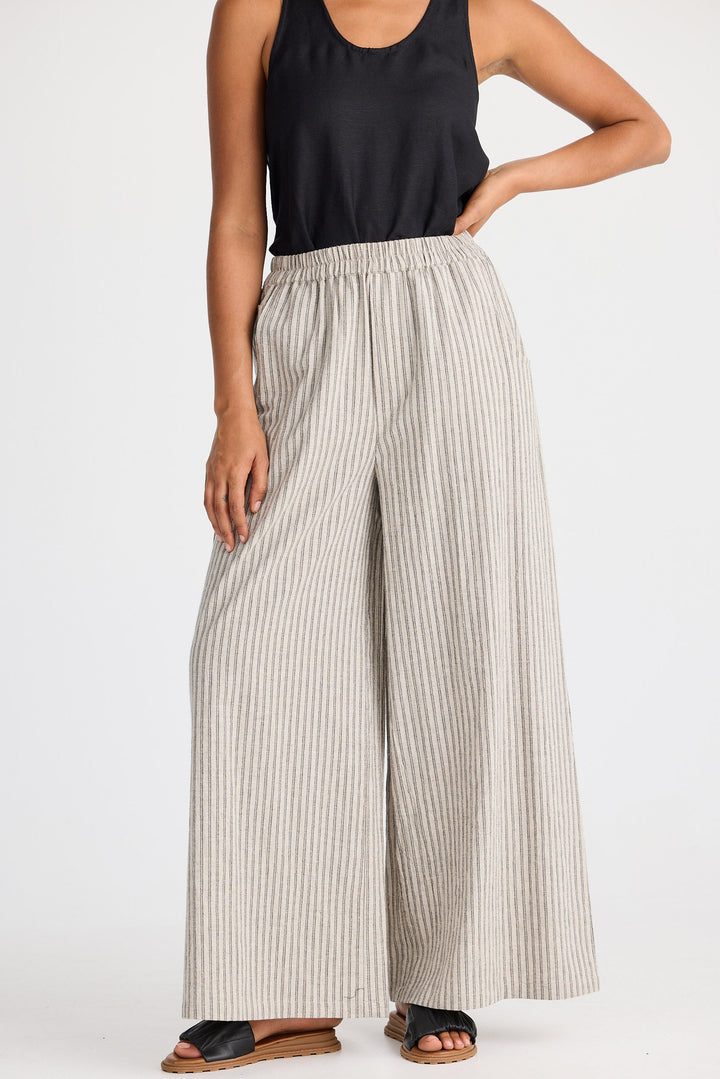 Woman wearing a black tank top and wide-leg striped pants on a white background