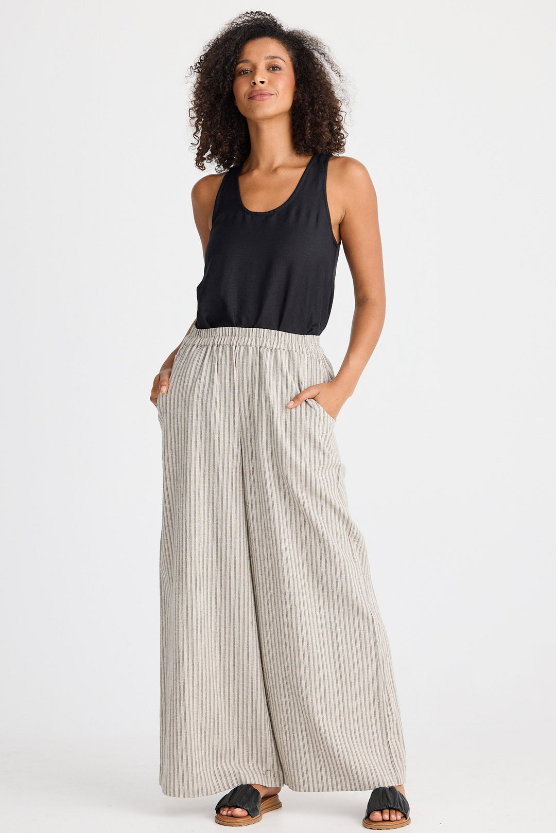 Woman wearing a black sleeveless top and striped pants on a white background