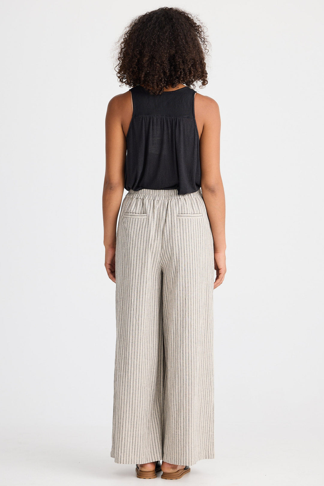 Person wearing a black sleeveless top and beige striped pants on a white background