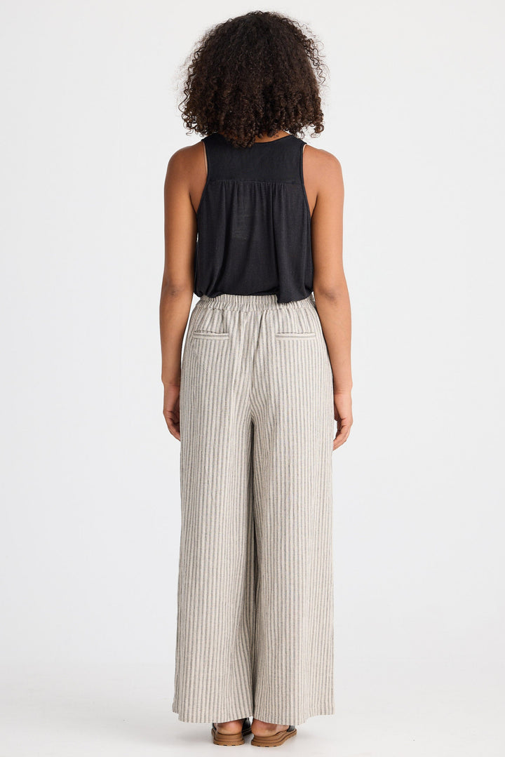 Person wearing a black sleeveless top and beige striped pants on a white background