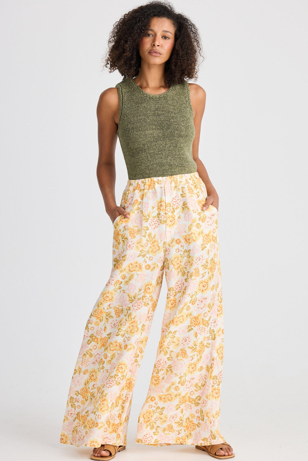 Woman wearing a green sleeveless top and yellow floral pants on a white background